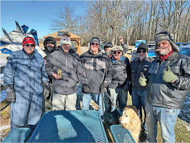 Seven people in winter clothing and a dog standing outdoors on a sunny day.