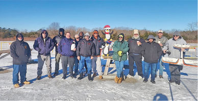 Group of people on a snowy field with a snowman under a clear blue sky.