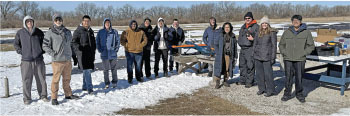 A group of people standing outside on snow near tables and benches.