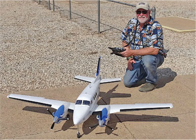 Man kneeling beside large model airplane with remote control on sunny day.