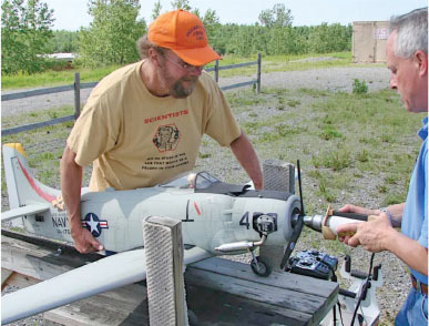 Two men preparing a model Navy aircraft outdoors.