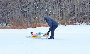 Person in winter clothes adjusting a model plane on snow.