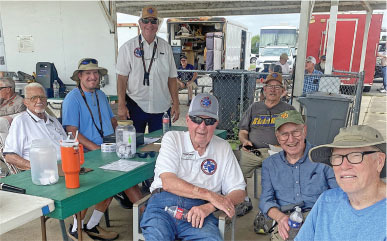 Group of smiling elderly men sitting at a table outdoors.