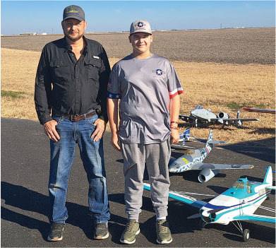 Two people standing on a road, with model airplanes on the ground.