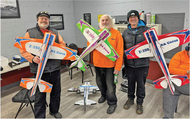 Three people holding colorful model planes indoors, smiling.