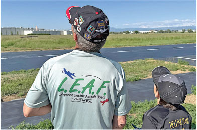 Man and child watching airfield, "L.E.A.F." logo on shirt.