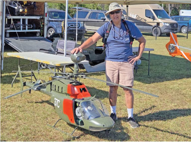 Man standing next to a large model helicopter on grass.