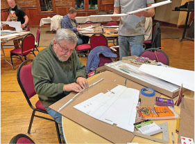 Man assembling model parts at a table with scattered supplies.