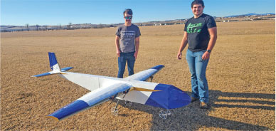 Two people standing on grass field with large model airplane.