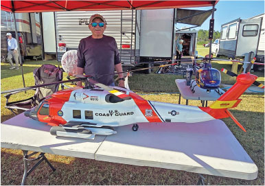 Man displaying a large model Coast Guard helicopter on a table under a red tent.