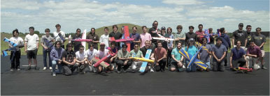 Group holding colorful model planes outdoors, under a cloudy sky.