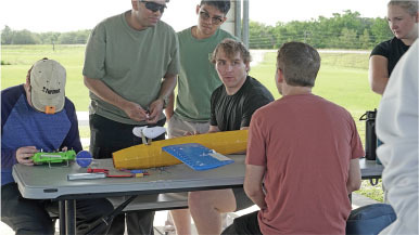 Group assembling model plane at a picnic table outdoors.