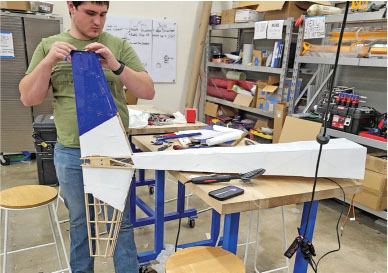 Man assembling a blue and white model airplane in a workshop.