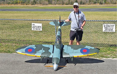 Man standing next to a large model airplane outdoors.