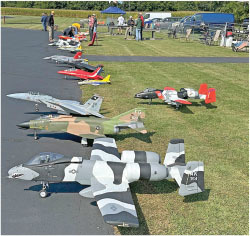 Model aircraft displayed on grass and pavement, people in the background.