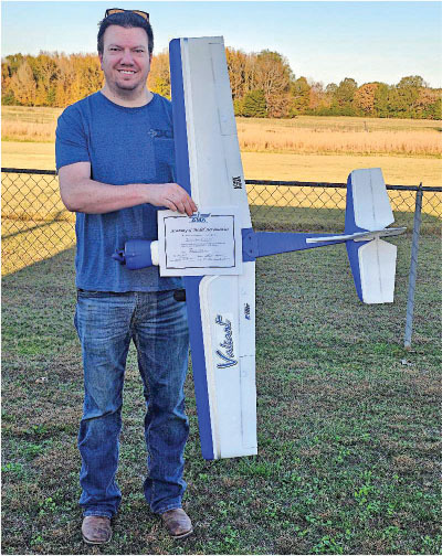 Man holding a large remote-controlled airplane and certificate, outdoors.