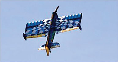 Aerobatic plane flying with checkered wings against blue sky.