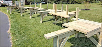 Wooden benches with armrests on grass near a road.