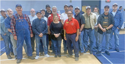 A group of people, mostly men, smiling indoors on a gymnasium floor.
