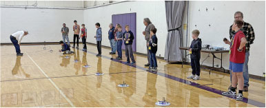 Kids and adults line up in a gymnasium, engaged with small flying toys.