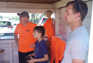 Men and a boy inside a shed, the boy holds a remote control.