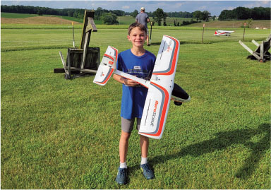 Boy holding a white model airplane on green grass.