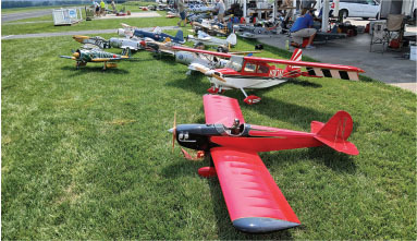Model airplanes on grass, people seated nearby under tents.