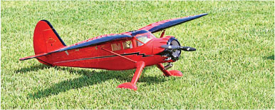 Red model airplane on green grass.
