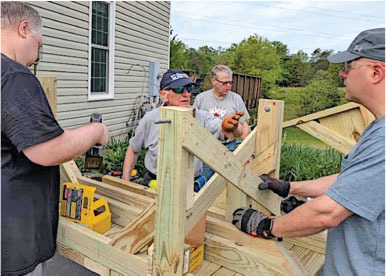 Four men building a wooden ramp, using tools, outside a house.
