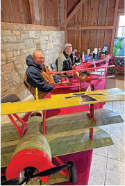 Two men sit behind a table with model airplanes, smiling in