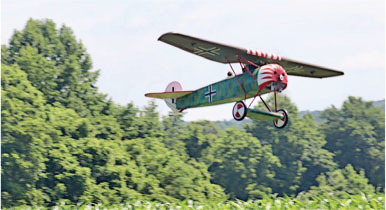 Vintage biplane with red stripes flying over green trees.