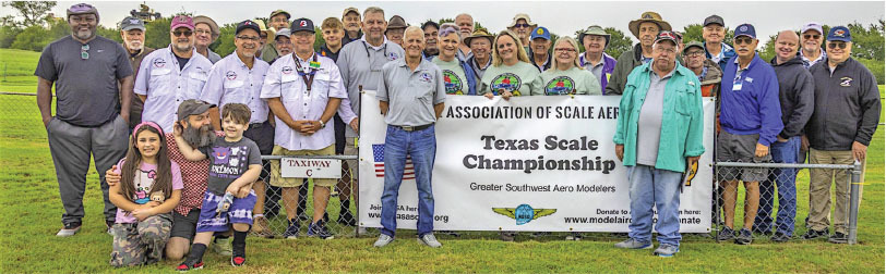 Group photo of people outdoors, behind a "Texas Scale Championship" banner.