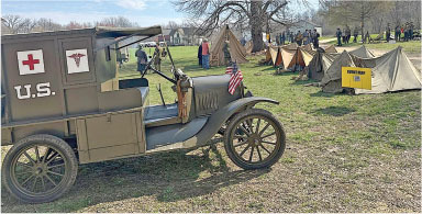 Historical U.S. military ambulance and tents on a grassy field with people in background.