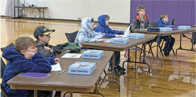 Children sitting at tables with boxes labeled "Take Control" in a gym setting.