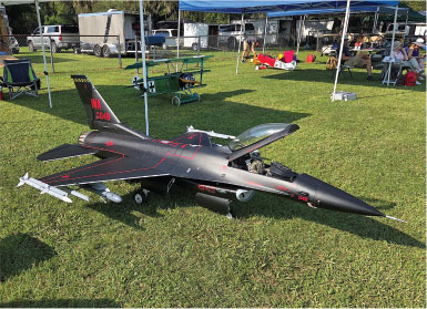 Model jet plane with red details on grass, surrounded by tents and people.