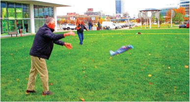 Man launching toy plane on green lawn, people in background.
