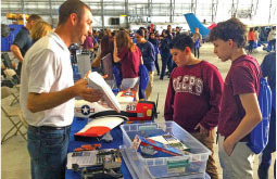 Man talking to two boys at a table with aviation materials in a hangar.