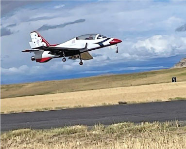 Jet in mid-flight over a runway, with cloudy skies in the background.