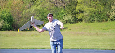 Man launching a small drone in a grassy field.