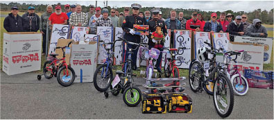 Group of people with Marines in uniform, surrounded by bikes and toy boxes outdoors.