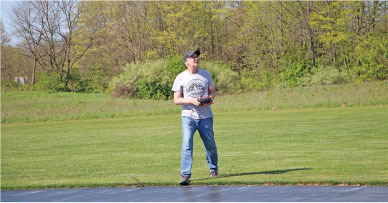 Man operating a remote control in a grassy field on a sunny day.