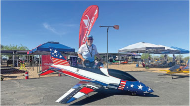 Man standing next to star-spangled model jet under a clear blue sky.