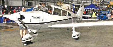 White Cherokee 180 airplane in a hangar with people nearby.