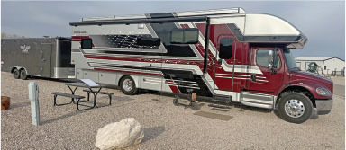Red and silver RV parked near a picnic area on gravel.