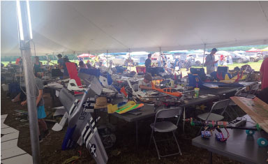 Large tent with people assembling model planes on tables.