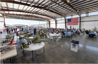 Airplane models and a crowd in a hangar with an American flag.