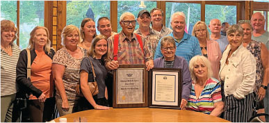 Group photo with two people holding framed certificates, smiling indoors.