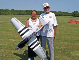 Elderly couple with a model plane on a grassy field.