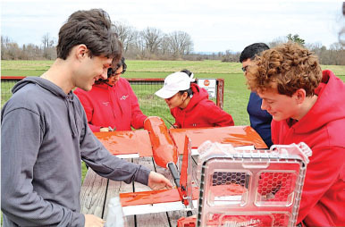 Group of young people assembling a model airplane outdoors.
