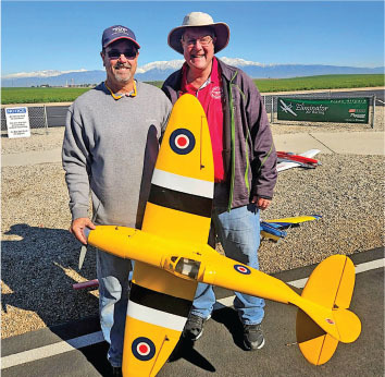 Two men smiling, holding a large yellow model airplane outdoors.
